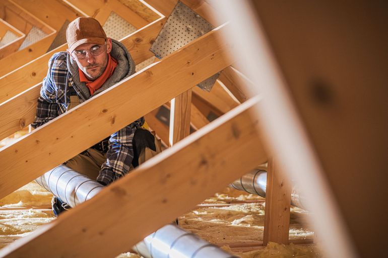 Worker in hard hat inspecting wooden roof framing in an attic under construction
