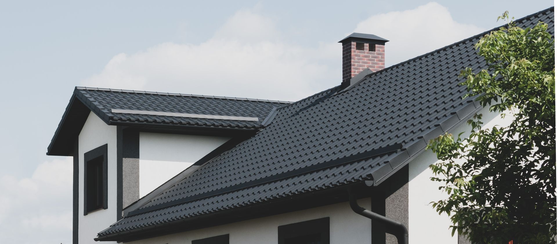 Une maison blanche avec un toit noir et une cheminée.