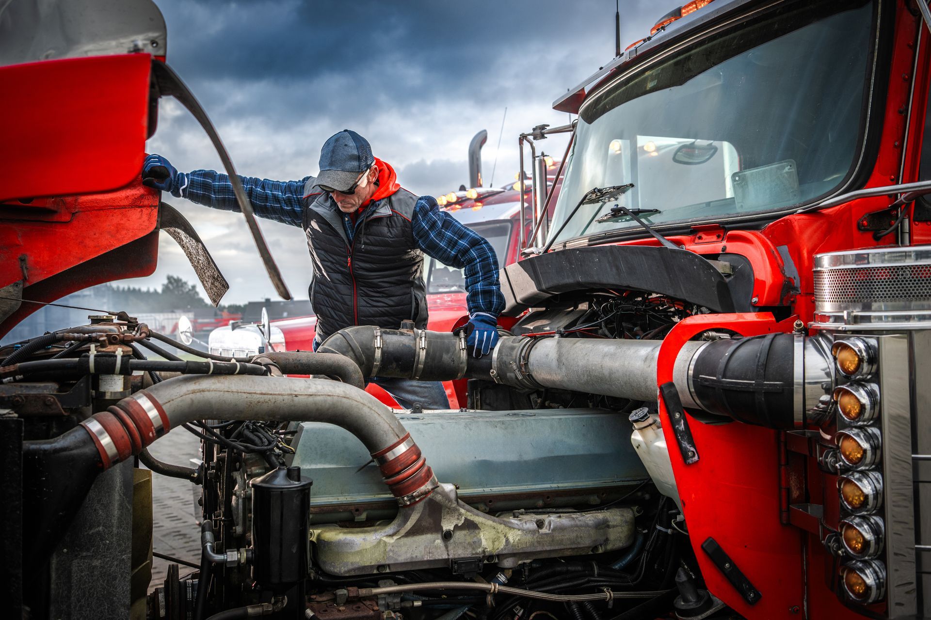 Truck mechanic inspecting the engine of a bright red semi-truck; outdoors, cloudy sky. Truck mechanic inspecting the engine of a bright red semi-truck; outdoors, cloudy sky.