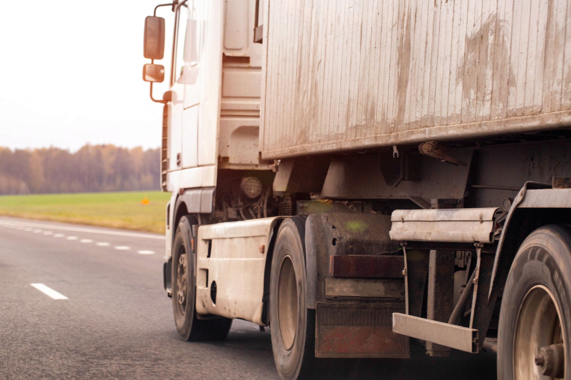 White semi-truck driving on a road with green field and trees in the background. White semi-truck driving on a road with green field and trees in the background.