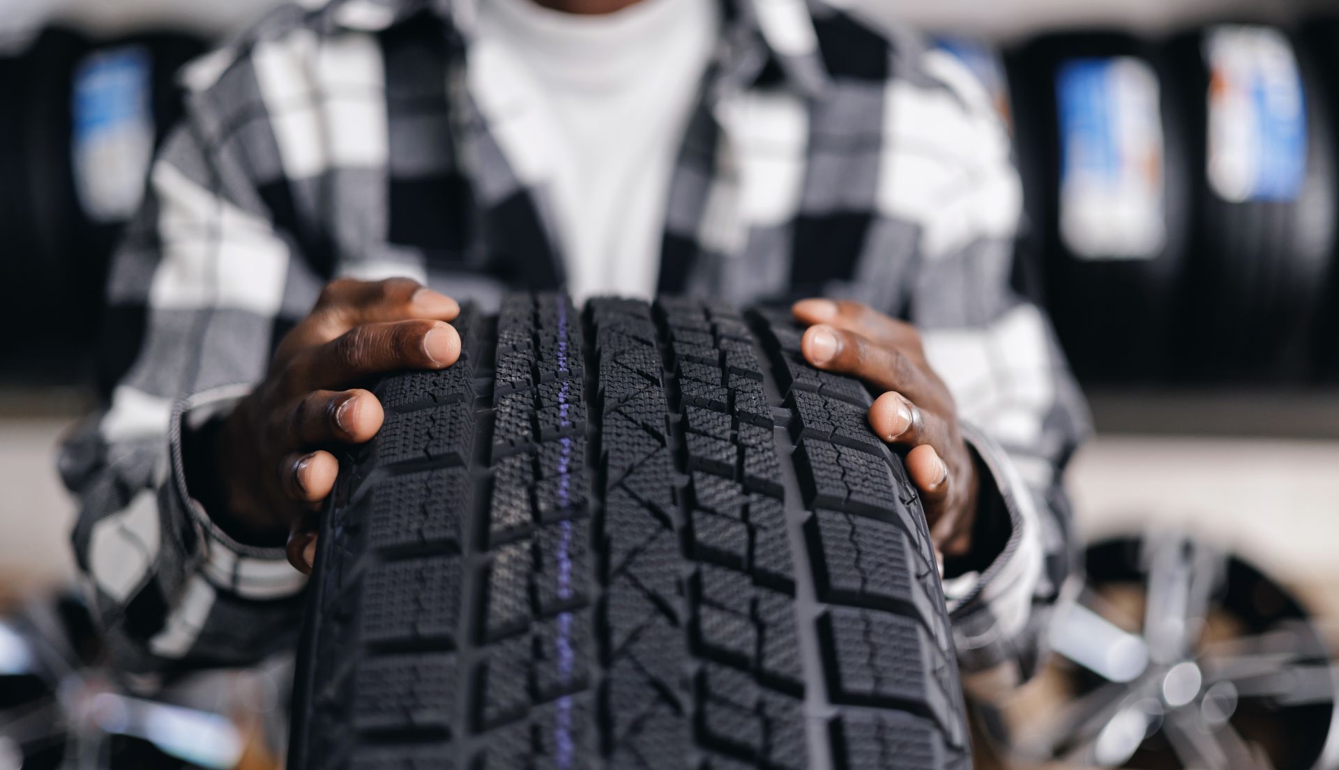 Person holding a tire, showcasing its tread. Tire shop setting, with other tires visible in the background. Person holding a tire, showcasing its tread. Tire shop setting, with other tires visible in the background.