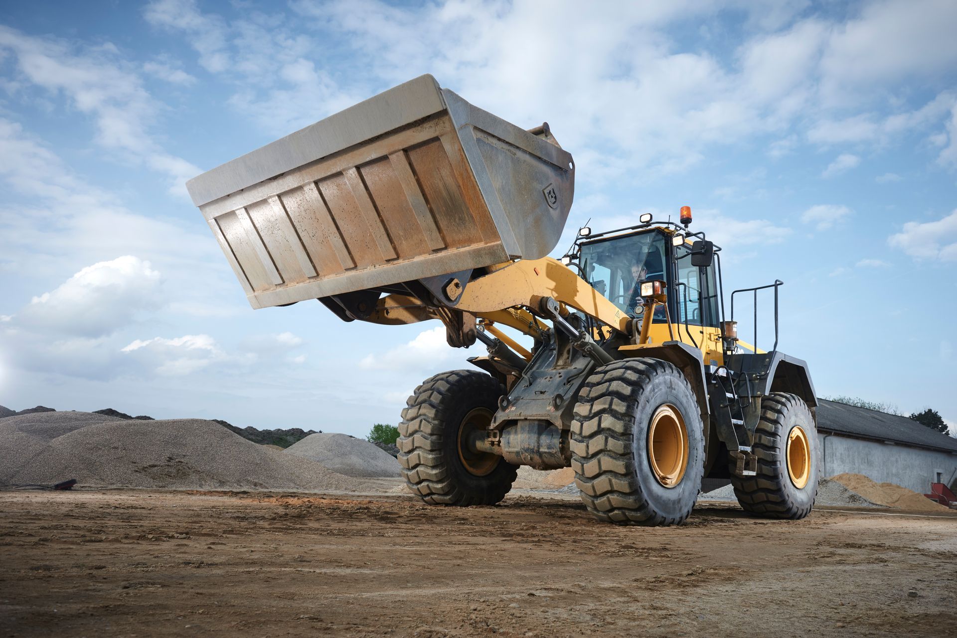 Yellow and black front-end loader with raised bucket on a construction site, blue sky in background. Yellow and black front-end loader with raised bucket on a construction site, blue sky in background.