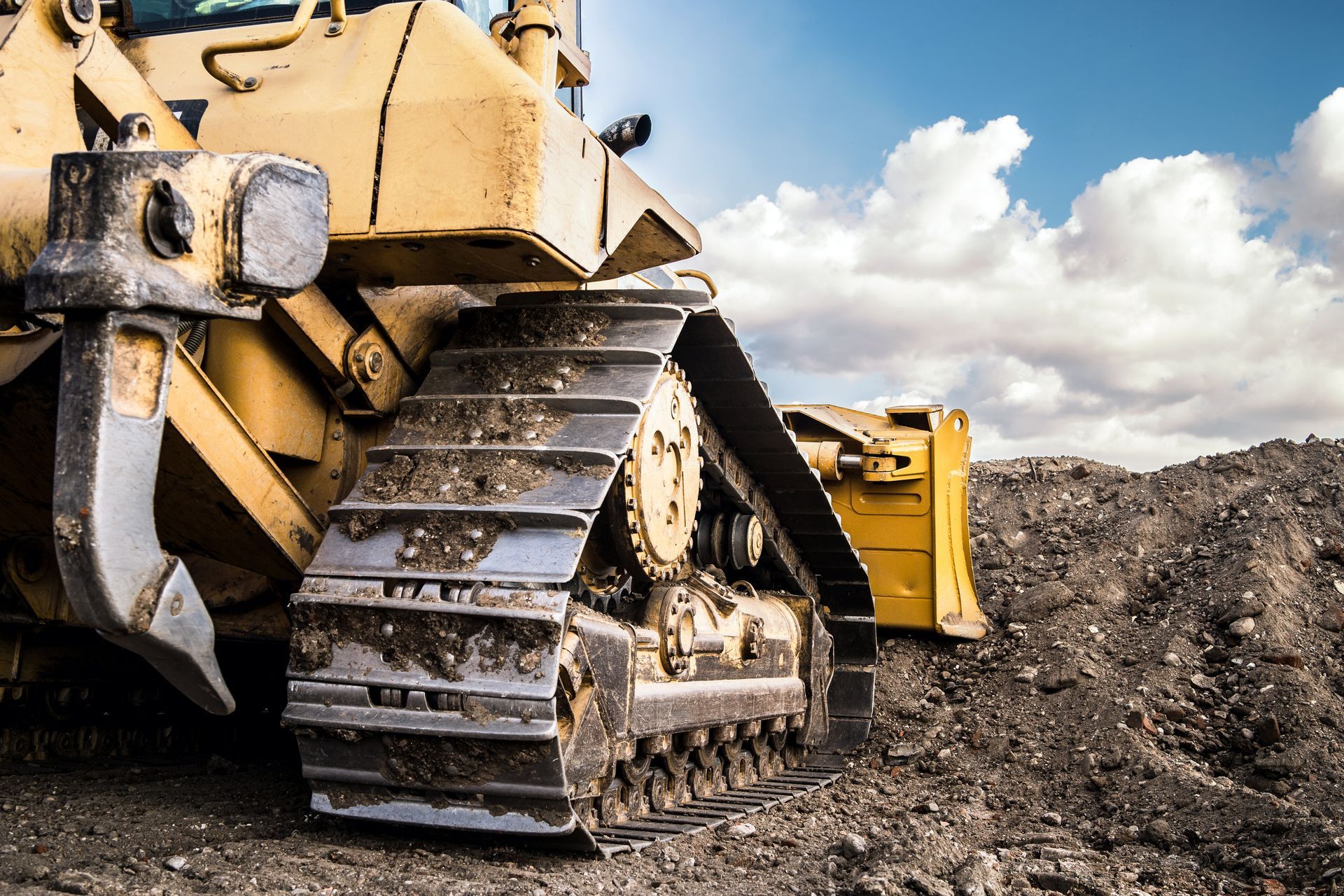 Yellow bulldozer on tracks, parked on a pile of dirt, against a cloudy blue sky. Yellow bulldozer on tracks, parked on a pile of dirt, against a cloudy blue sky.