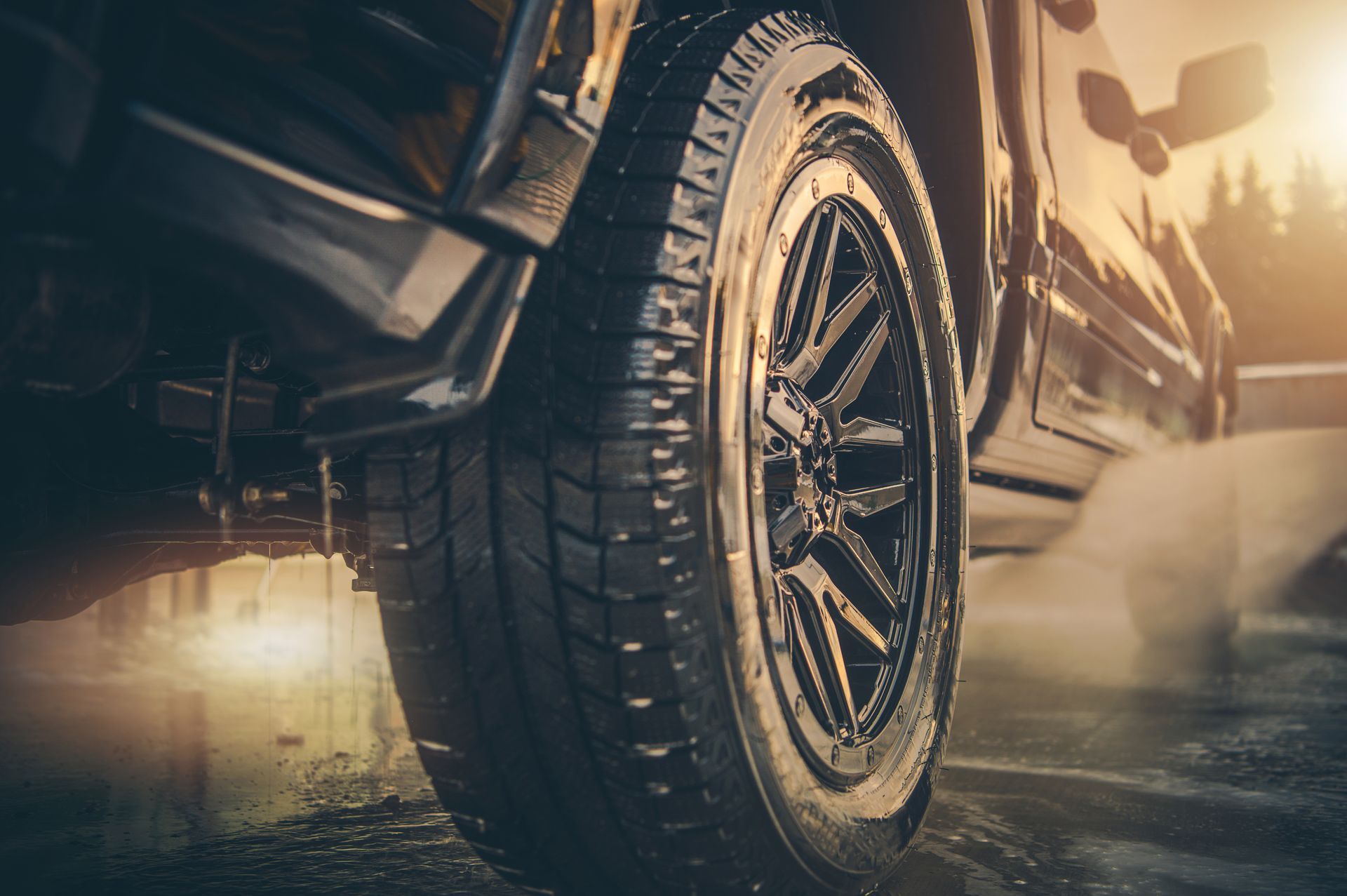 Close-up of a black truck tire, angled upward. Tire tread is visible, with sunlight highlighting details. Close-up of a black truck tire, angled upward. Tire tread is visible, with sunlight highlighting details.