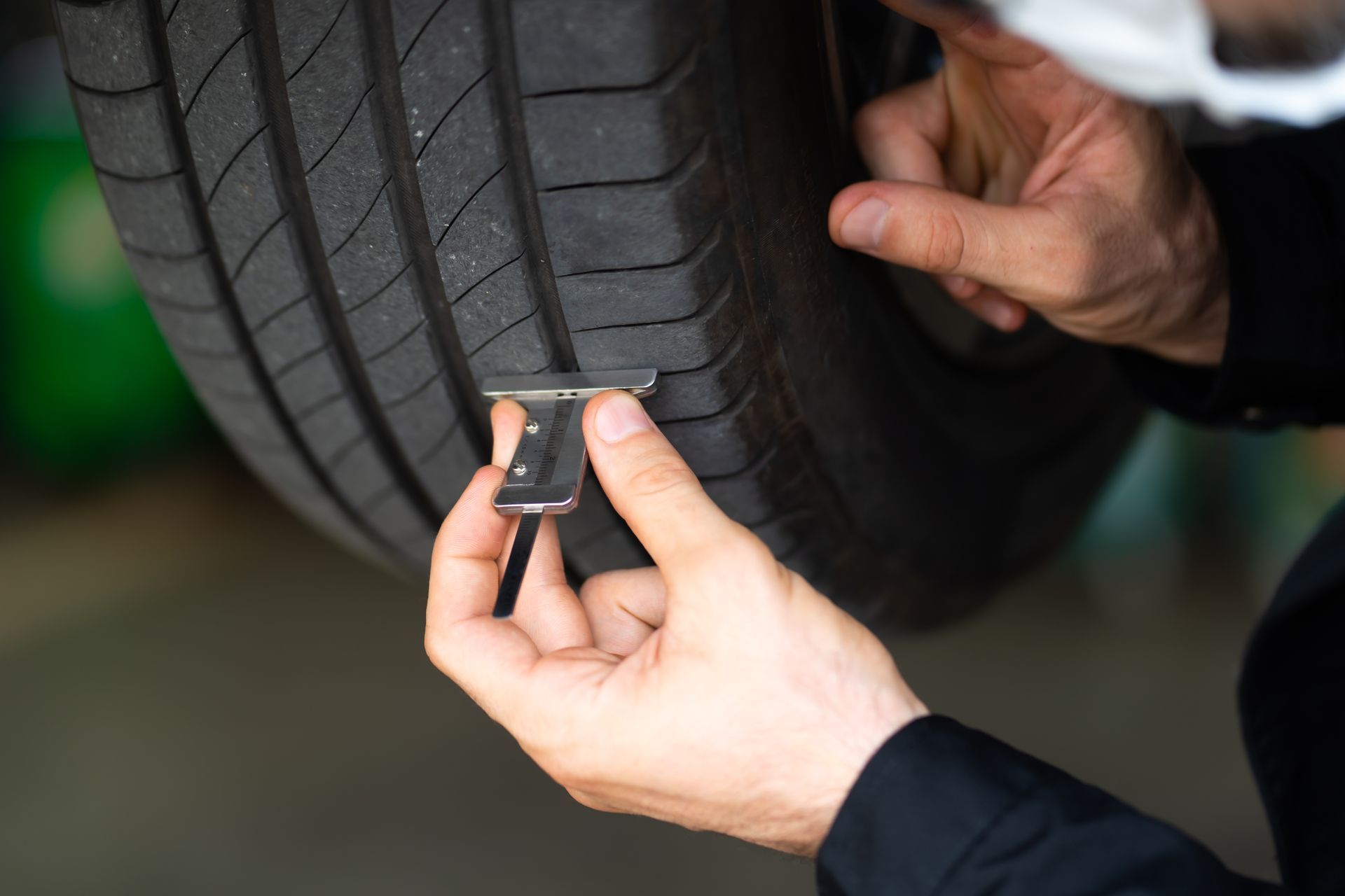 Person using a tire tread depth gauge to check the tire wear on a car's tire.