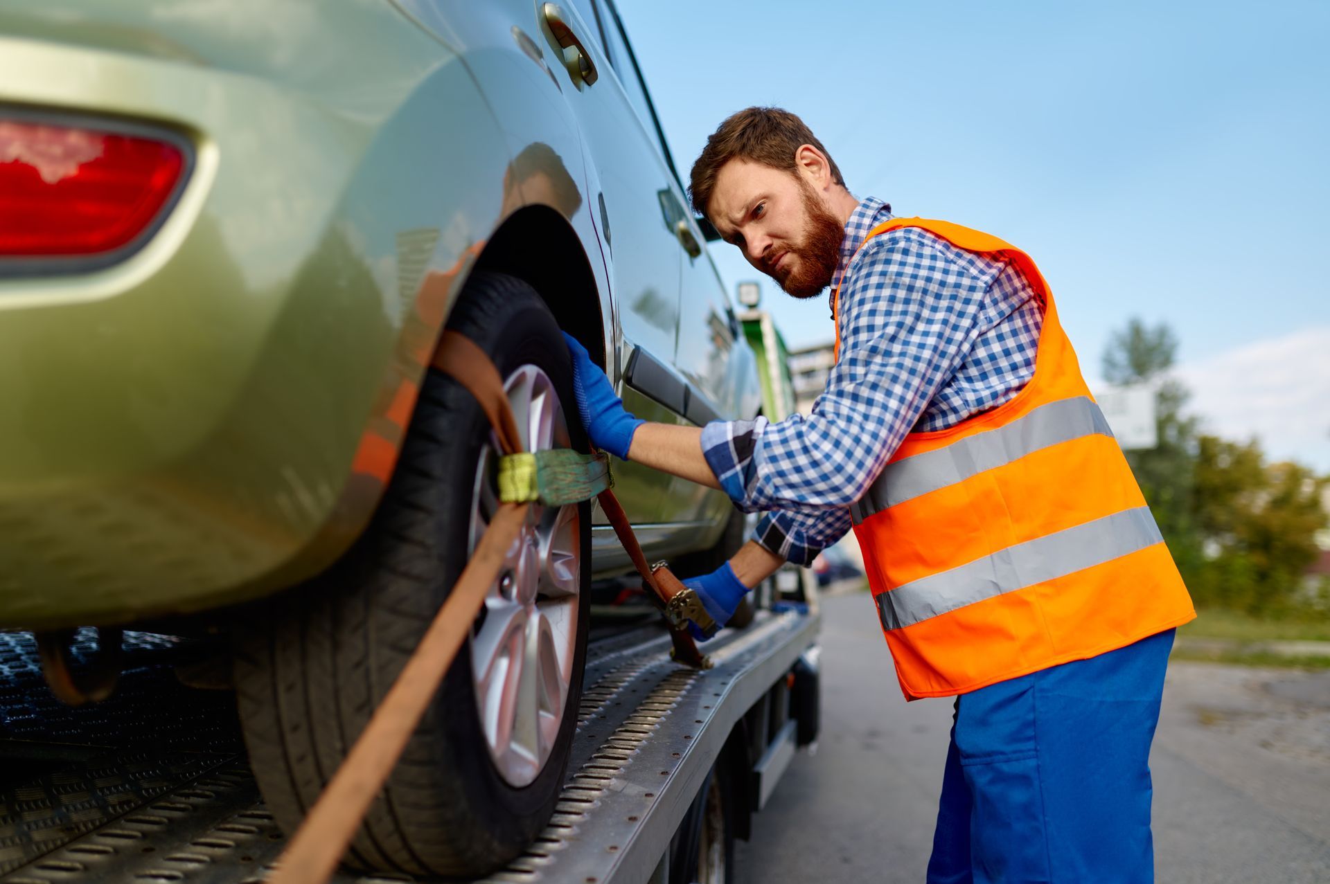 Tow truck operator secures a vehicle with straps. Man in safety vest and gloves. Tow truck operator secures a vehicle with straps. Man in safety vest and gloves.