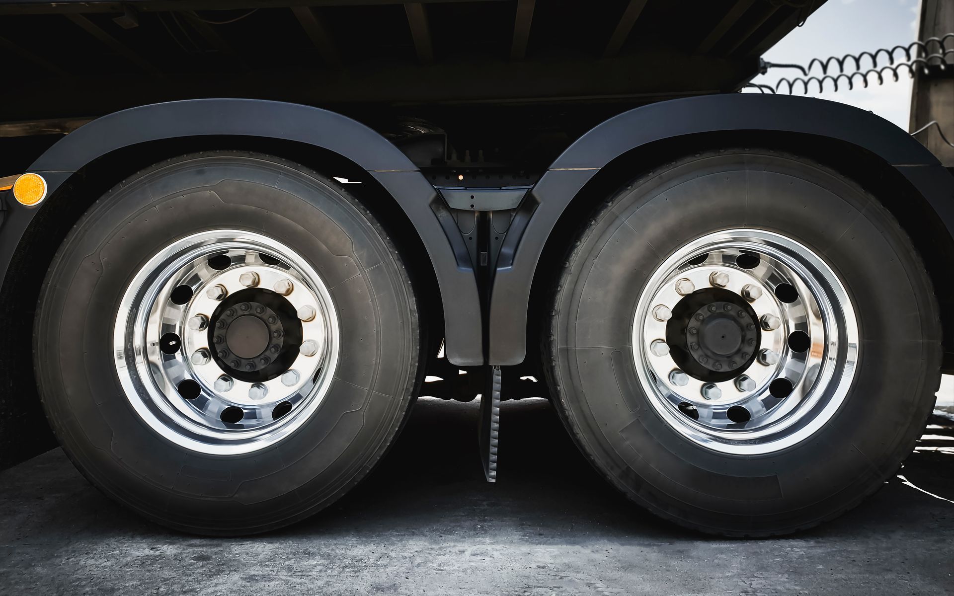 Two black truck tires with chrome rims under a black fender. Two black truck tires with chrome rims under a black fender.