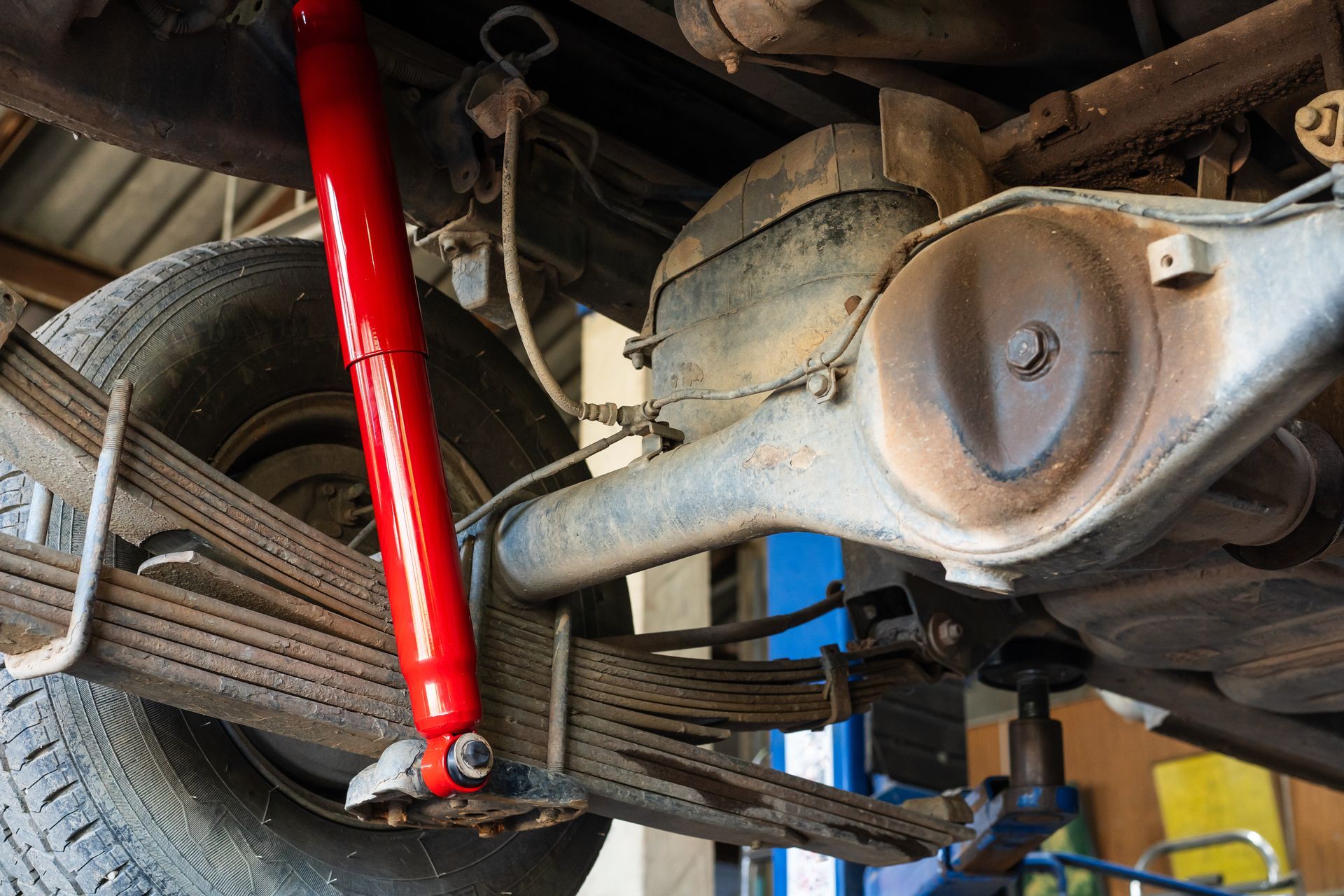 Red shock absorber installed on a vehicle's rear axle with leaf springs.