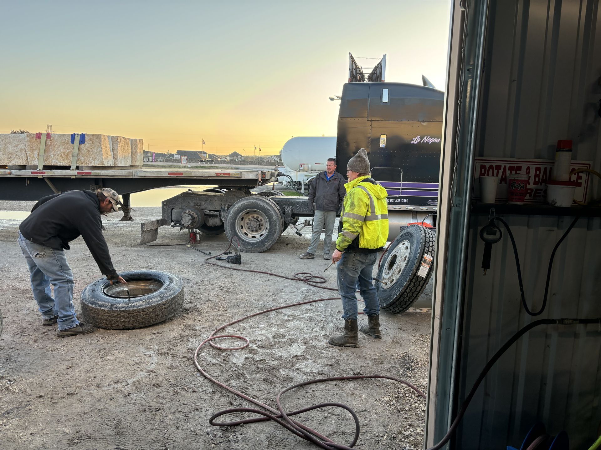 Three people working on a truck tire in a repair bay. One person is handling the tire while others observe. Three people working on a truck tire in a repair bay. One person is handling the tire while others observe.