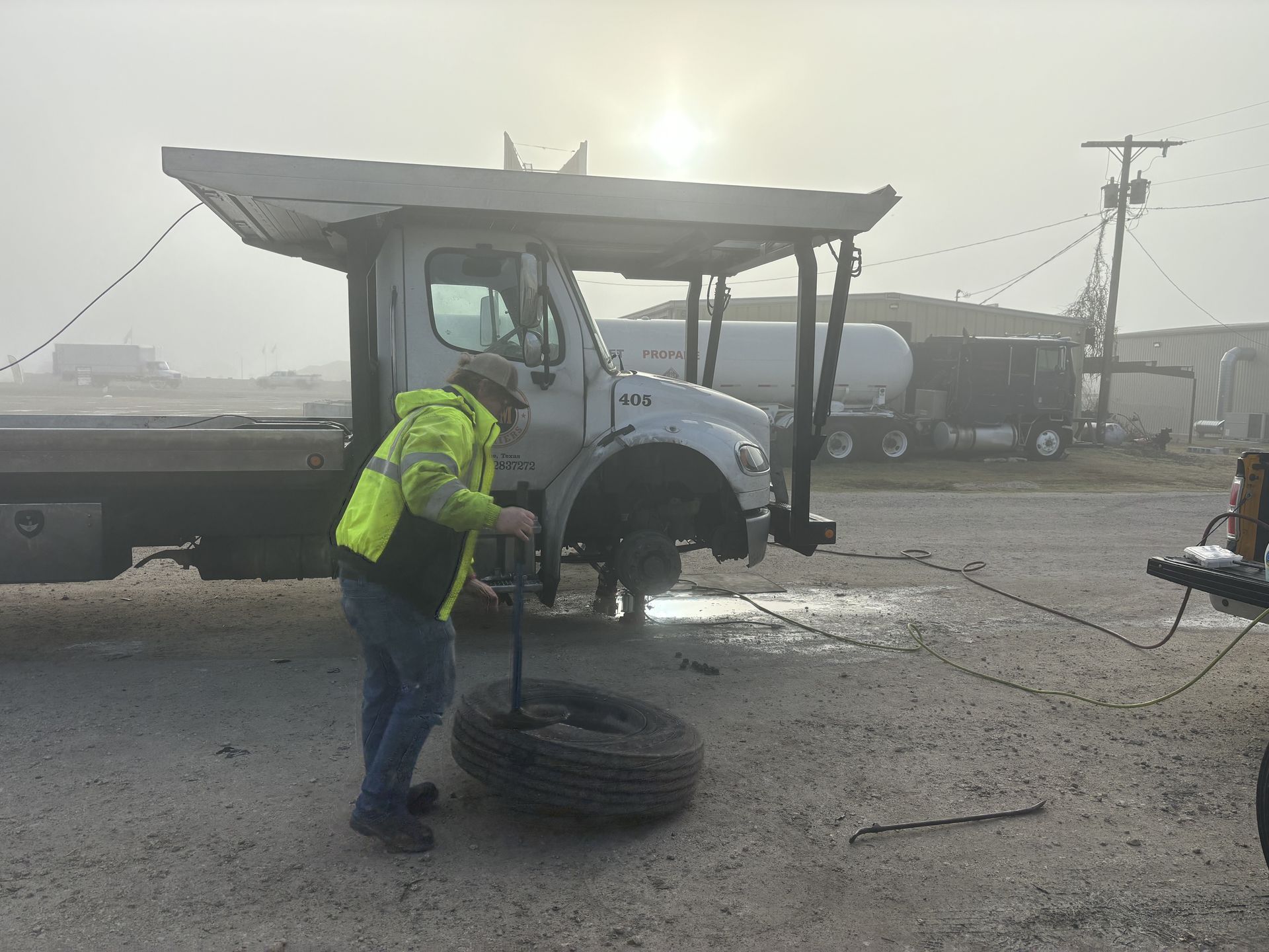 A person changing a tire on a tow truck on a foggy day. A person changing a tire on a tow truck on a foggy day.