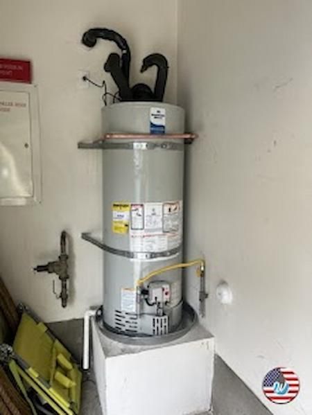 Water heater in a utility room with pipes, a yellow shutoff valve, and cleaning tools leaning nearby