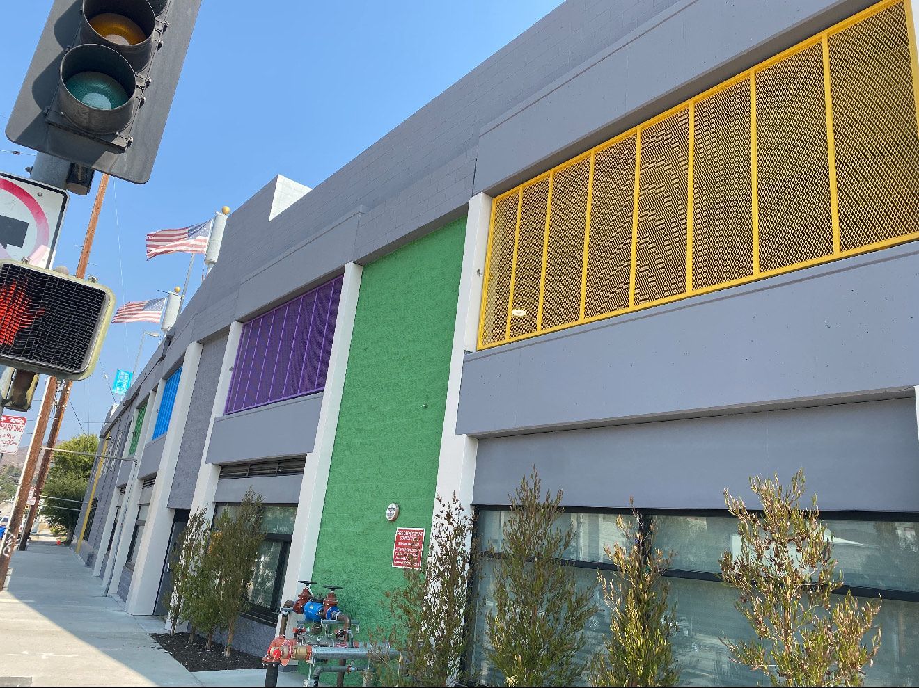 A grey street-level building with a green accent wall, a purple panel, and a large yellow metal grate, seen from a sidewalk.