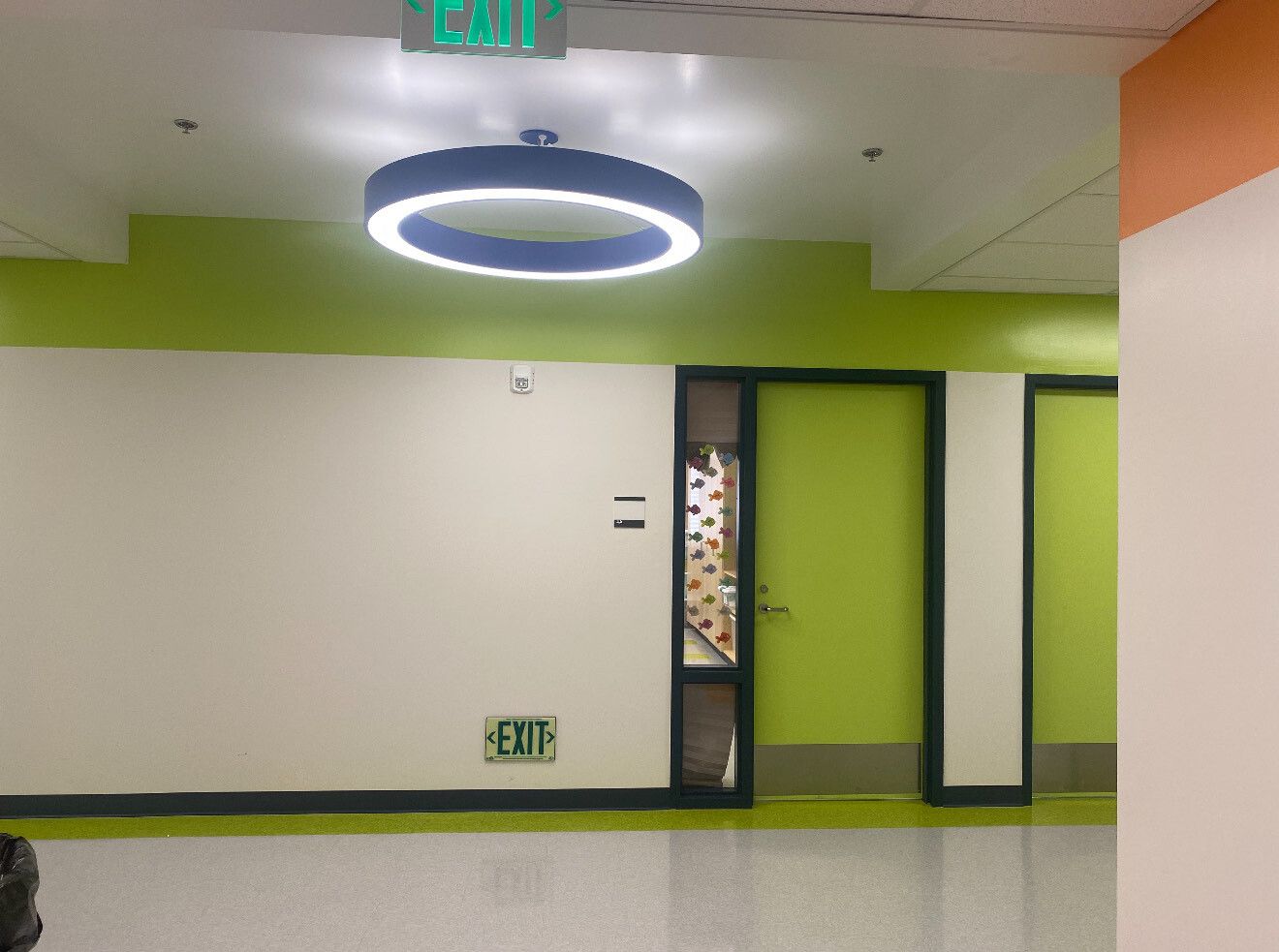 A bright hallway with light green walls, a circular LED ceiling light, and green doors.