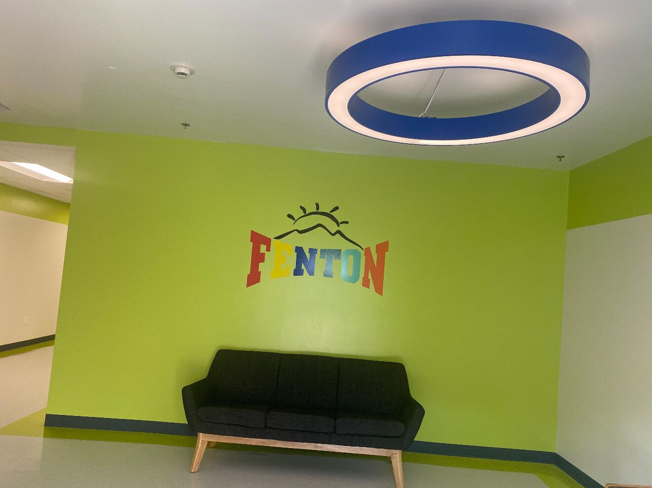 A black sofa sits against a lime-green wall in a hallway, featuring a colorful 