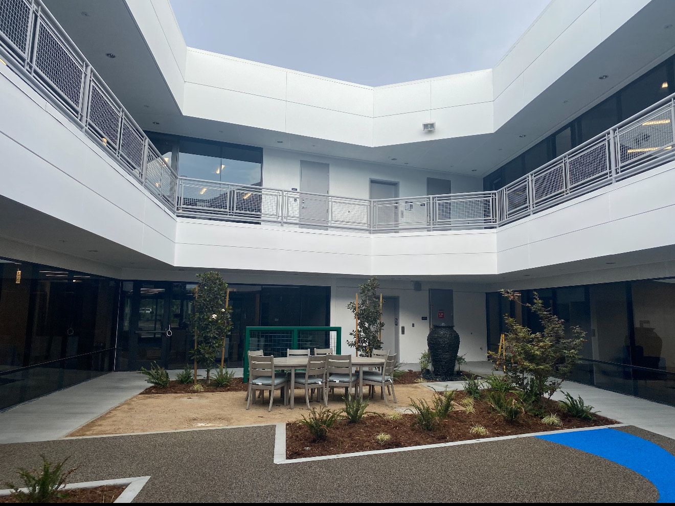 A white two-story courtyard building with a central patio area featuring seating, gravel landscaping, and a black fountain.