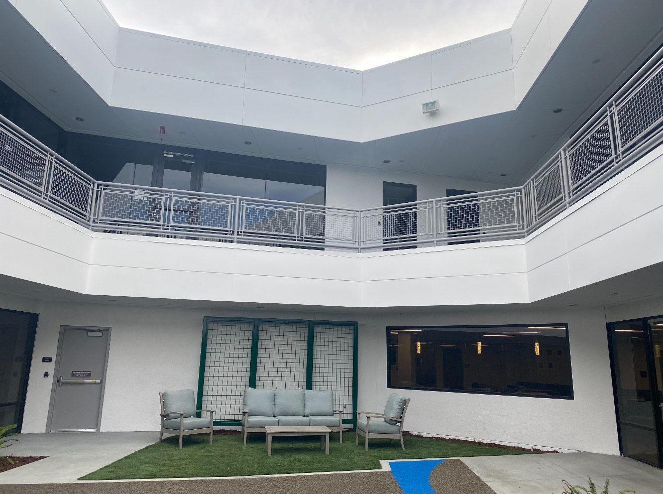 A white, two-story open-air courtyard with metal railings, featuring a small patch of grass with outdoor seating.