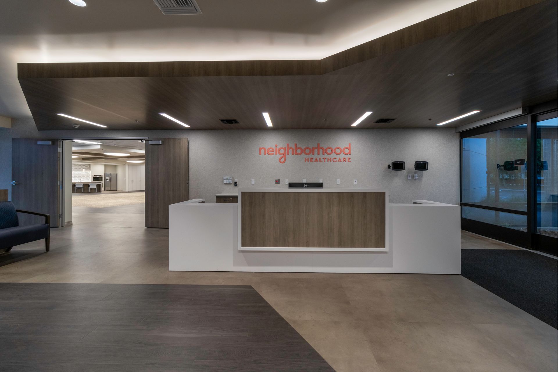 A modern office lobby with a reception desk, wood-paneled ceiling, and a sign reading