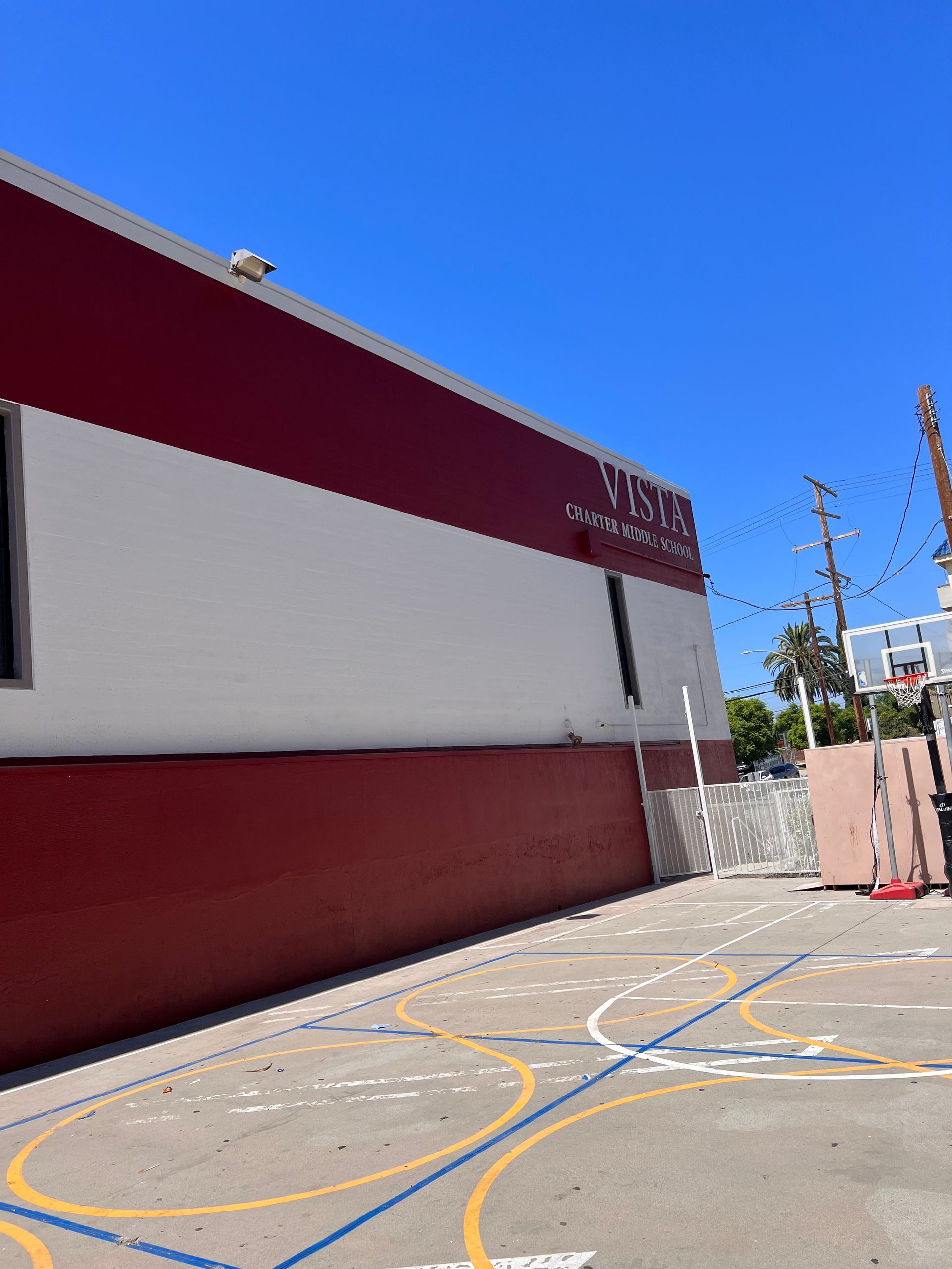 A red and white school building next to a playground with painted circles and a basketball hoop under a clear blue sky.
