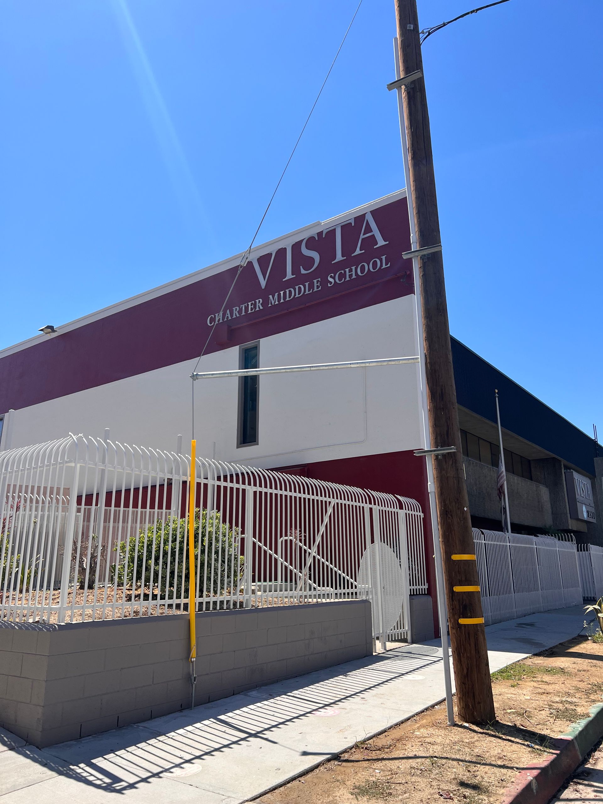 Vista Elementary School building with white and maroon walls, seen behind a white fence under a bright blue sky.