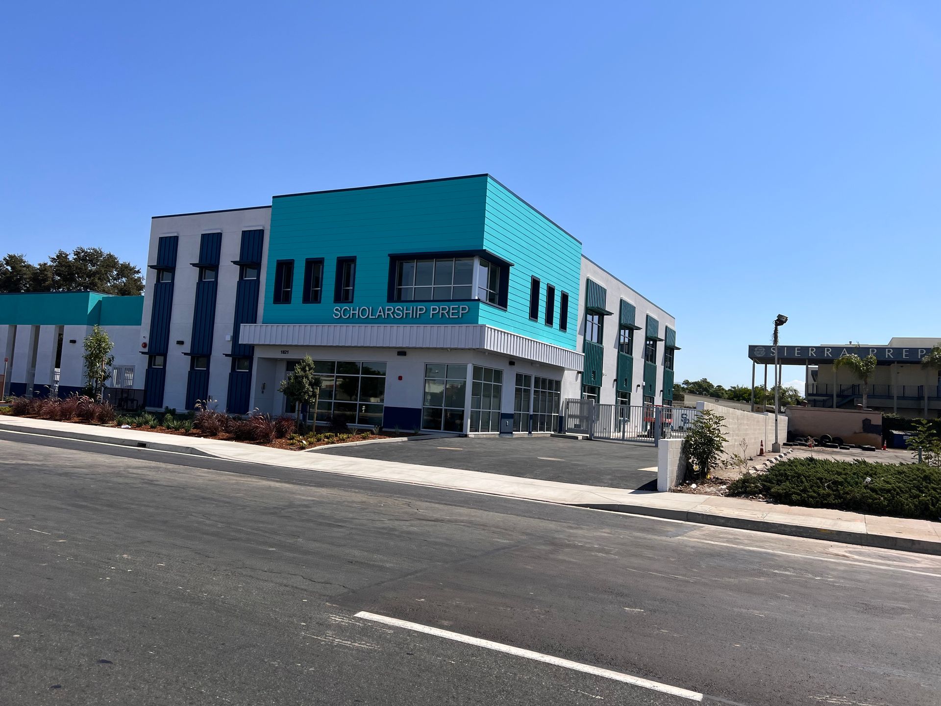 A modern two-story building with turquoise and white accents and blue vertical panels stands beside an asphalt road.