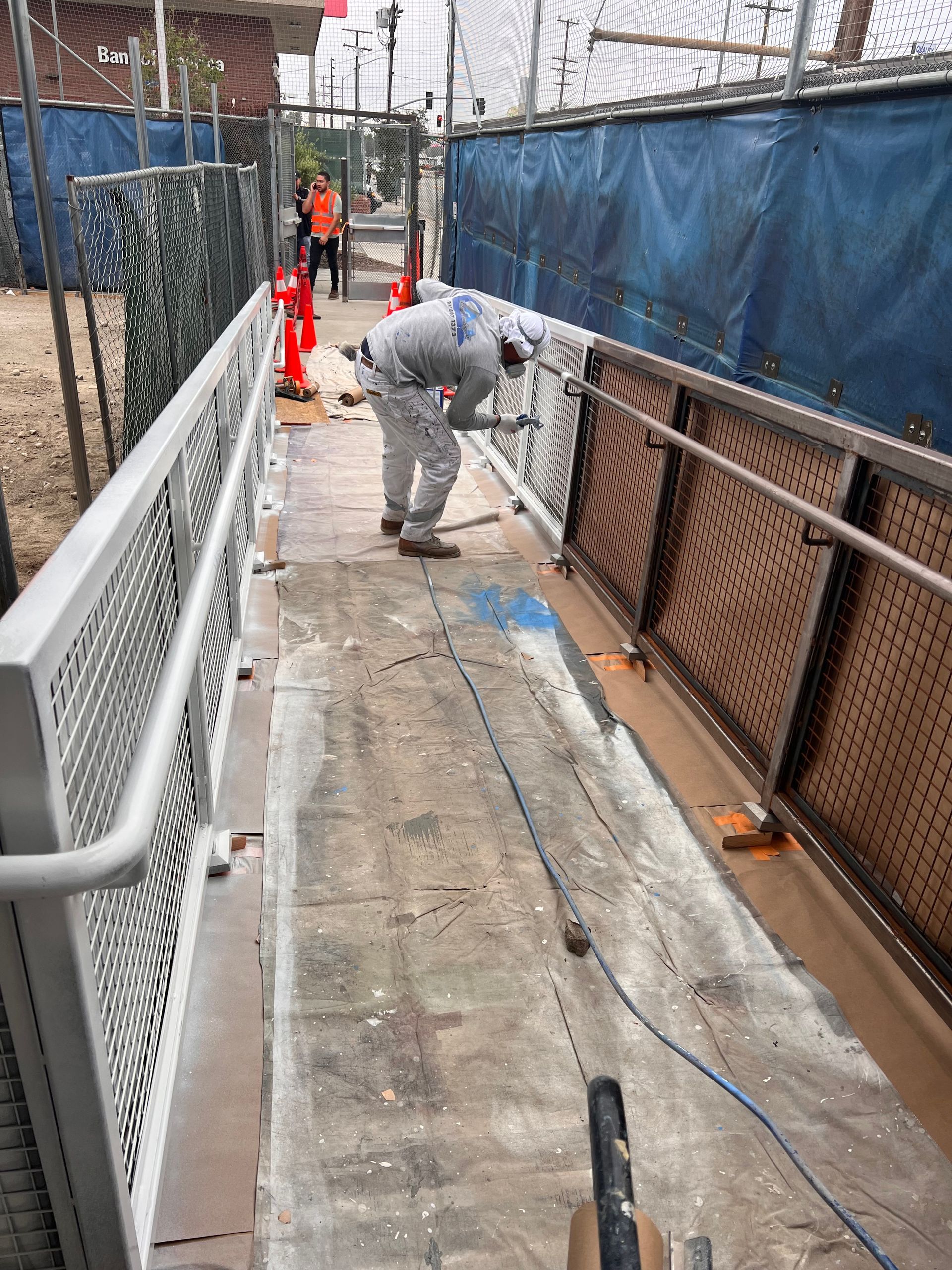 A worker wearing protective gear uses a tool to clean or refinish a metal ramp walkway at a construction site.