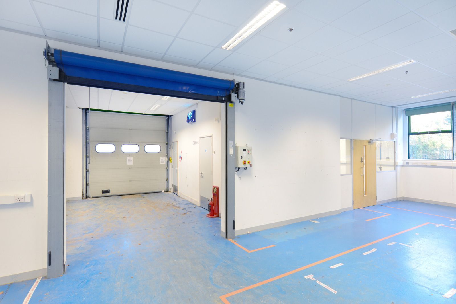 Empty industrial room with blue floor, white walls, and a wide doorway to a garage area
