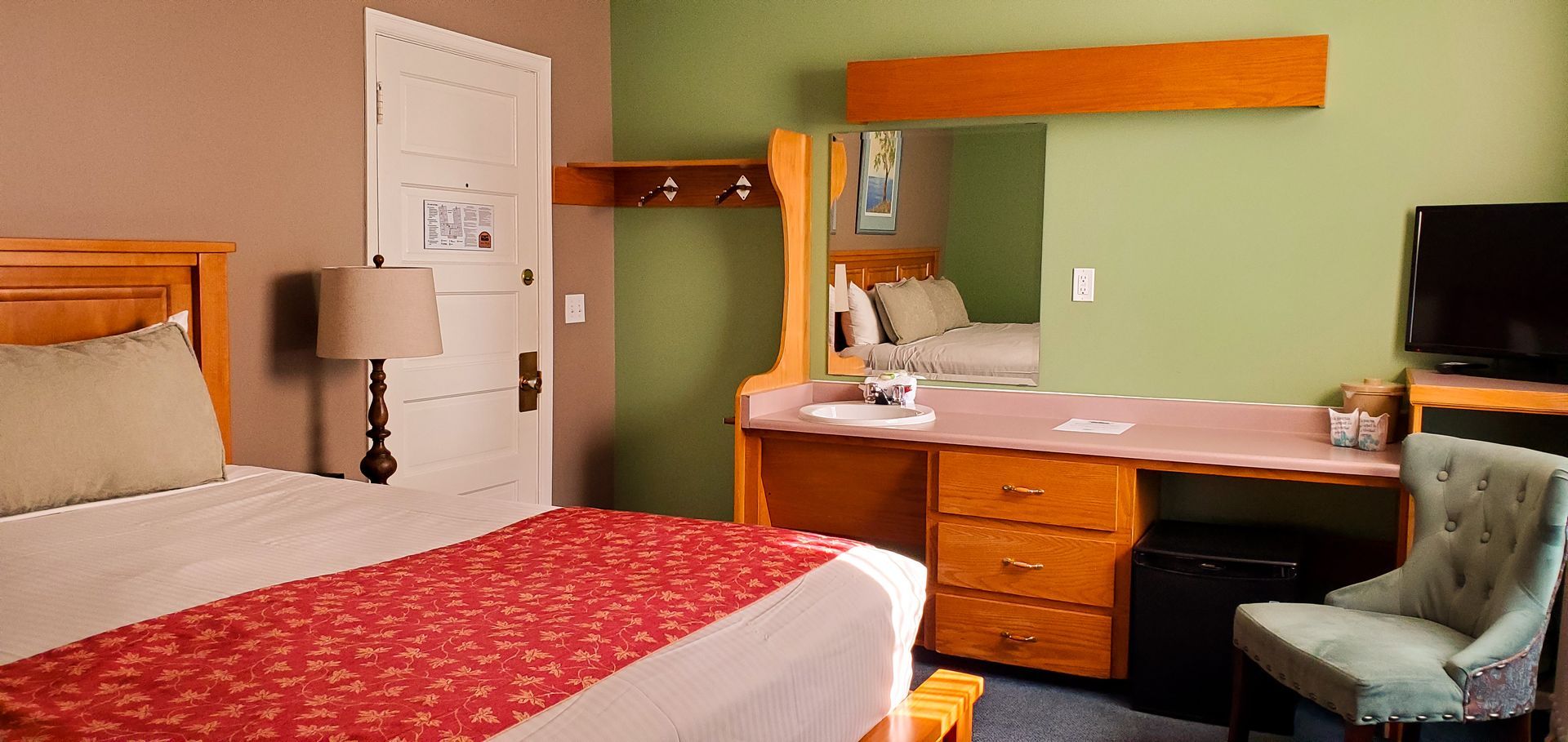A hotel room with a king size bed , desk , chair and television.