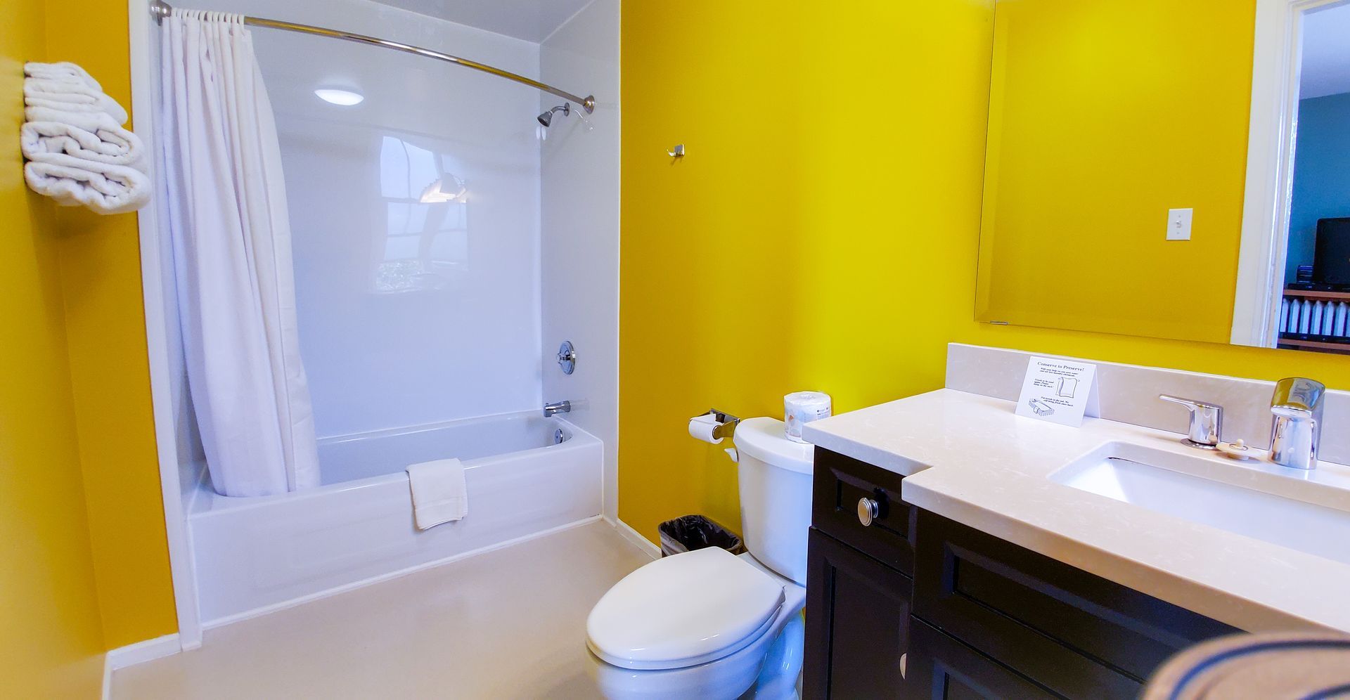 A bathroom with yellow walls , a toilet , sink and bathtub.