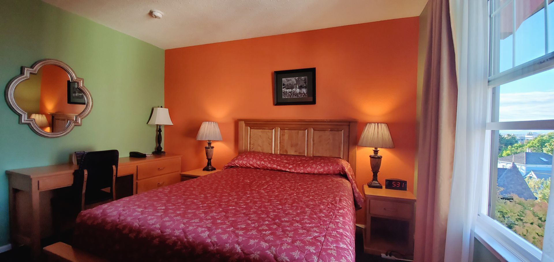 A hotel room with a bed , lamps , a mirror and a window.