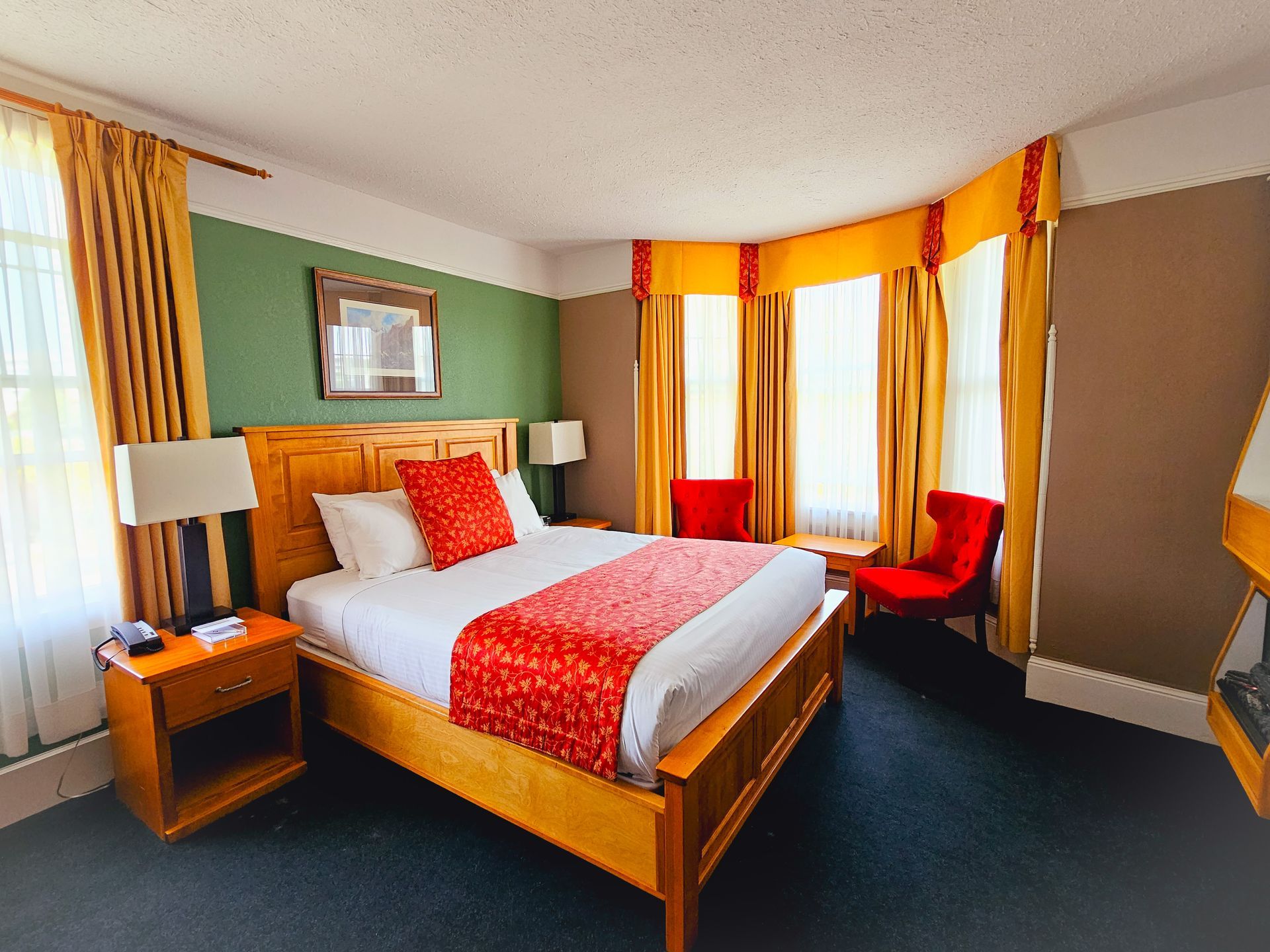 A hotel room with a king size bed , chairs , lamps and curtains.