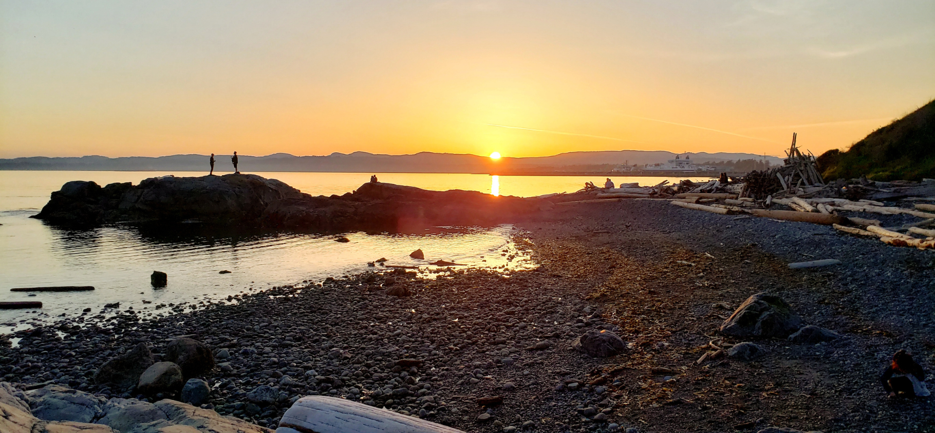 The sun is setting over the ocean on a rocky beach.