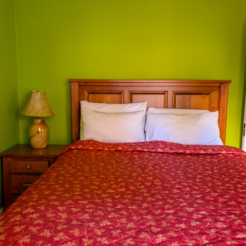 A bedroom with a bed , nightstand , lamp and green walls.