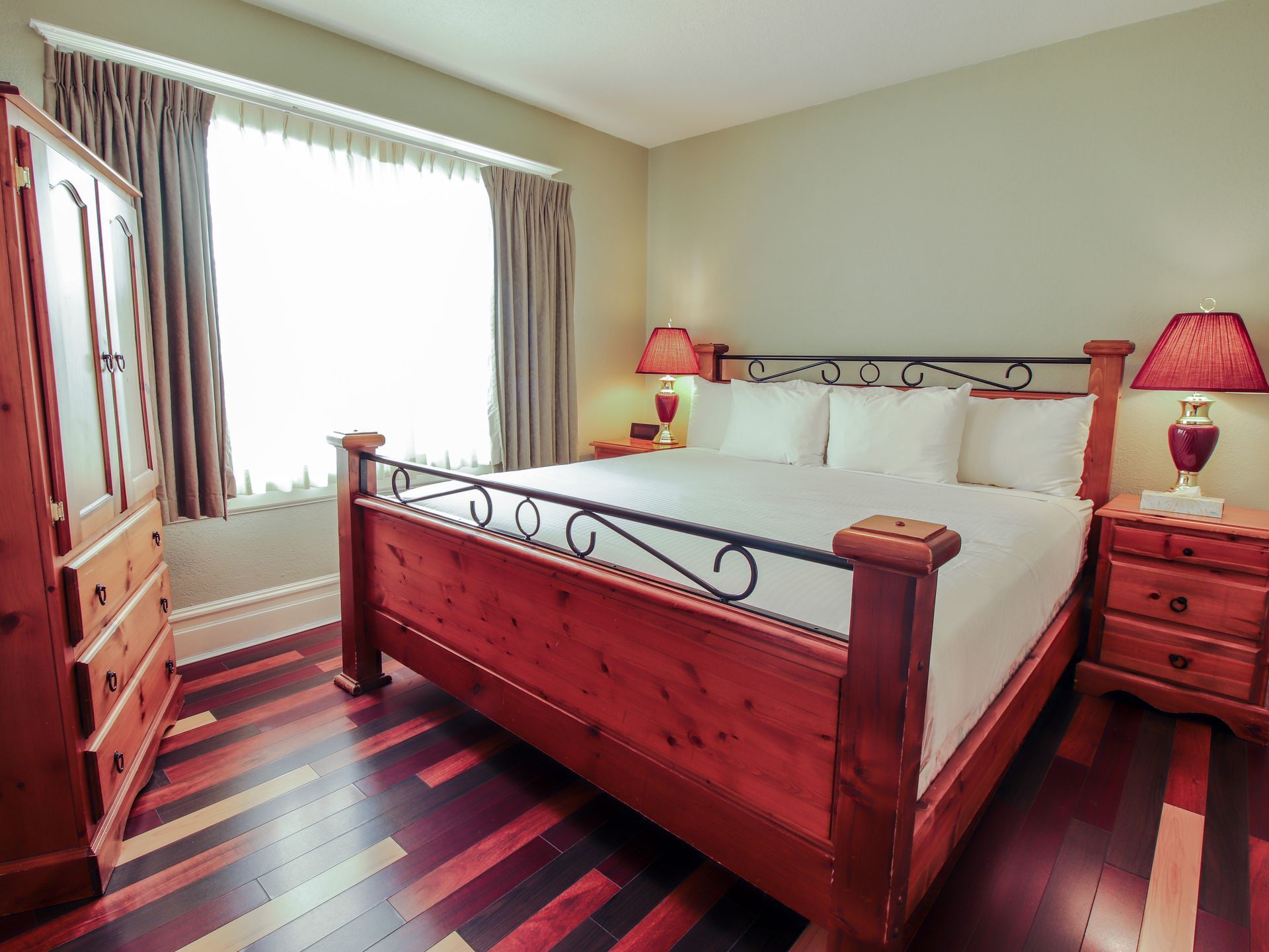 A bedroom with a king size bed , two nightstands , a dresser and a window.