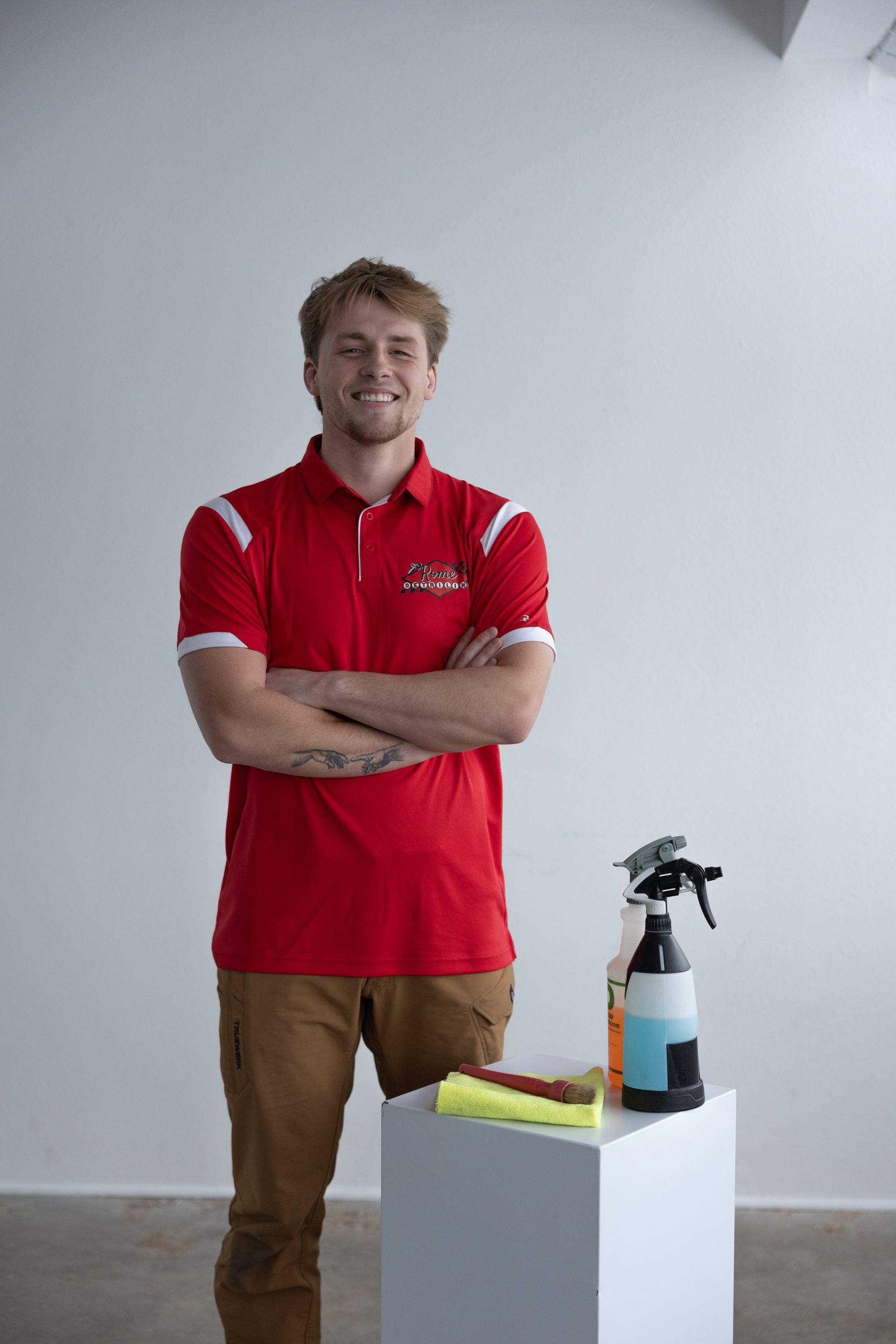 Man in red shirt standing beside cleaning spray bottles and supplies on a white pedestal