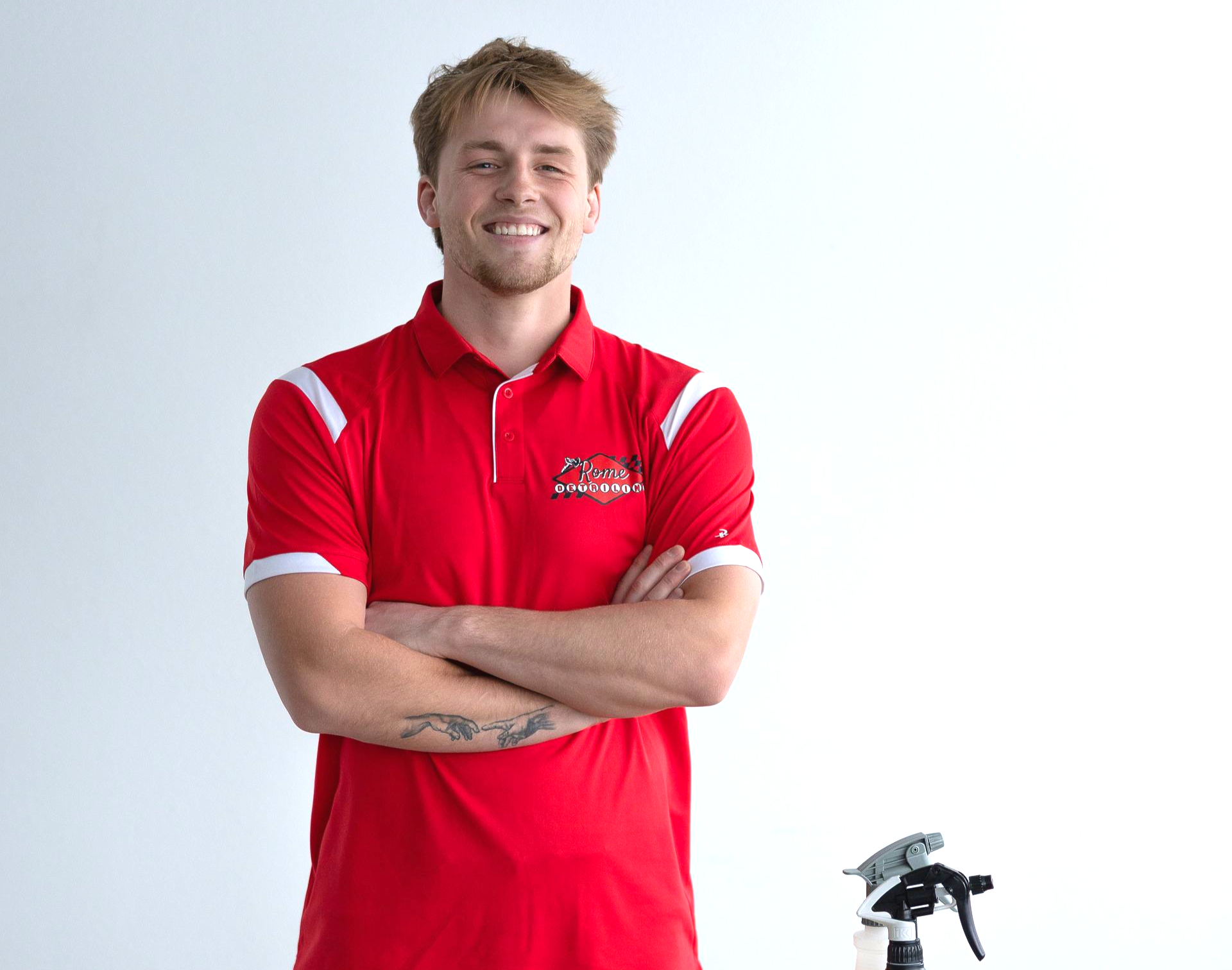 Smiling person in a red polo shirt with arms crossed, standing against a white background.