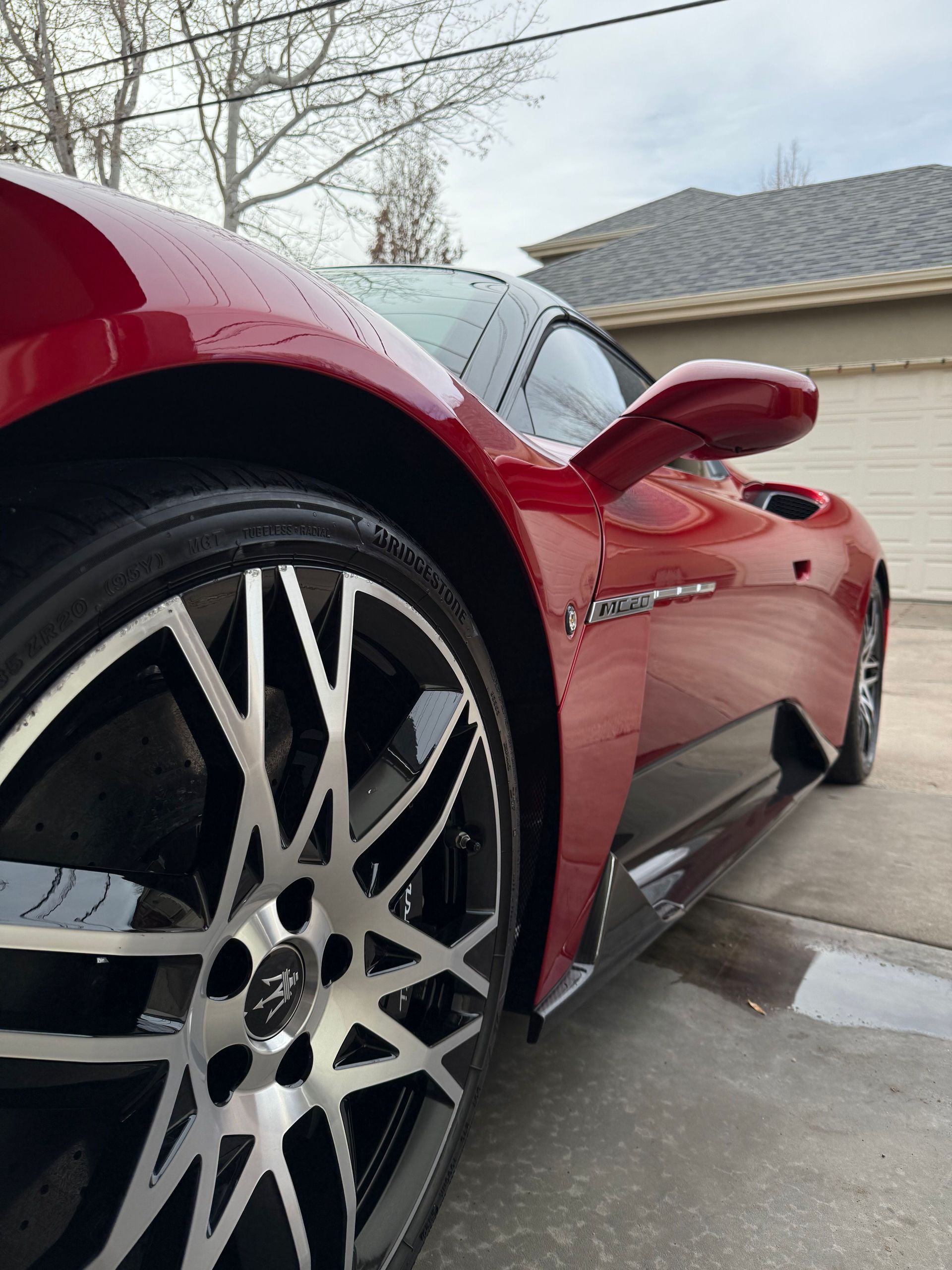 Red sports car close-up with large alloy wheel on a driveway near a garage