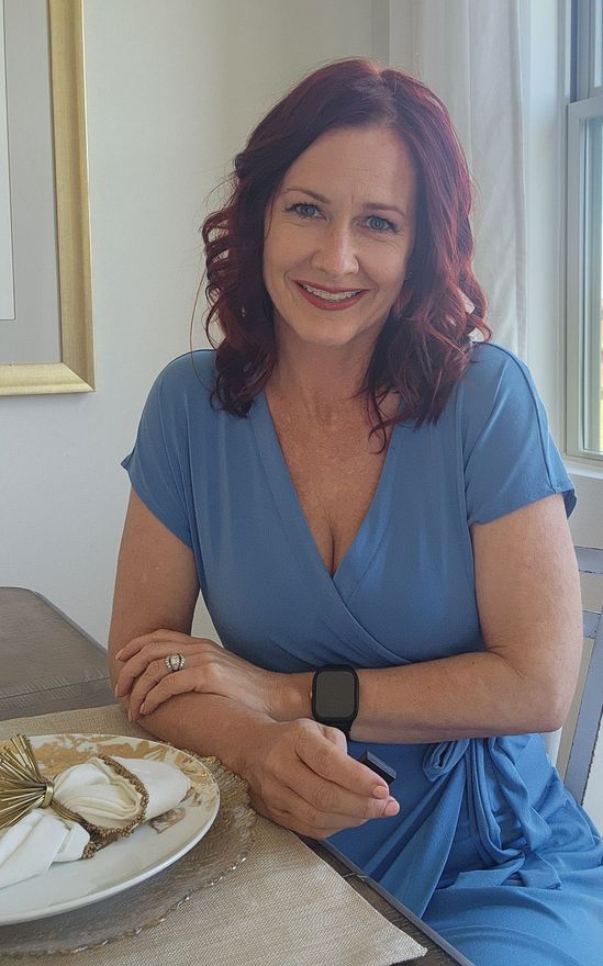 Heather Watson Realtor All Phase Real Estate A woman is sitting at a desk with a laptop and a vase of flowers.