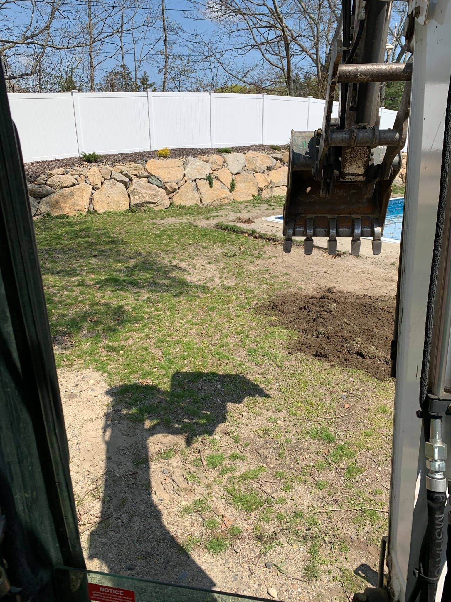 A bulldozer is digging a hole in the grass in a backyard.