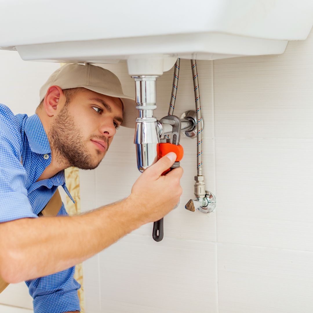 A man is fixing a sink with a wrench.