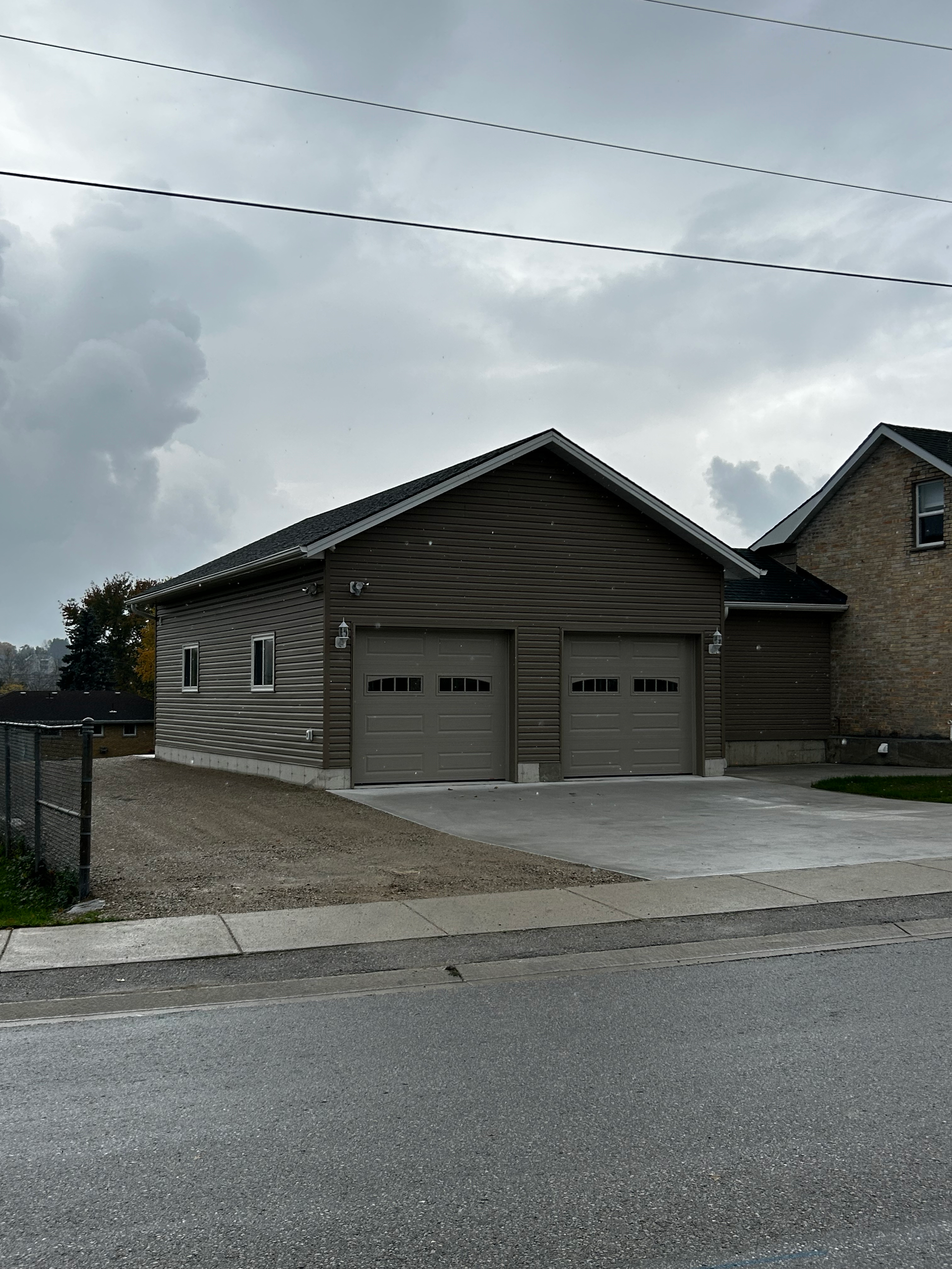 A garage with two garage doors is next to a house on a cloudy day.