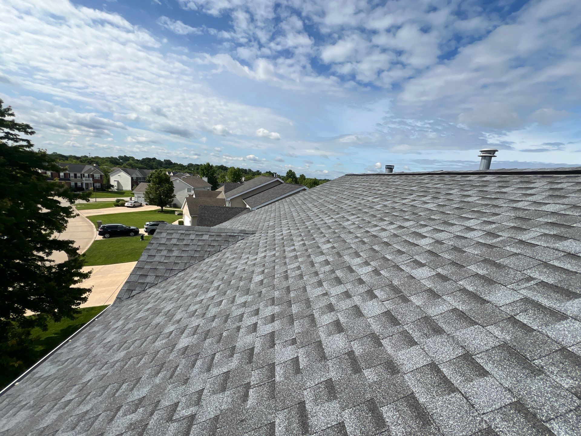 Gray asphalt shingle roof on a house, with a cloudy sky and neighborhood view.