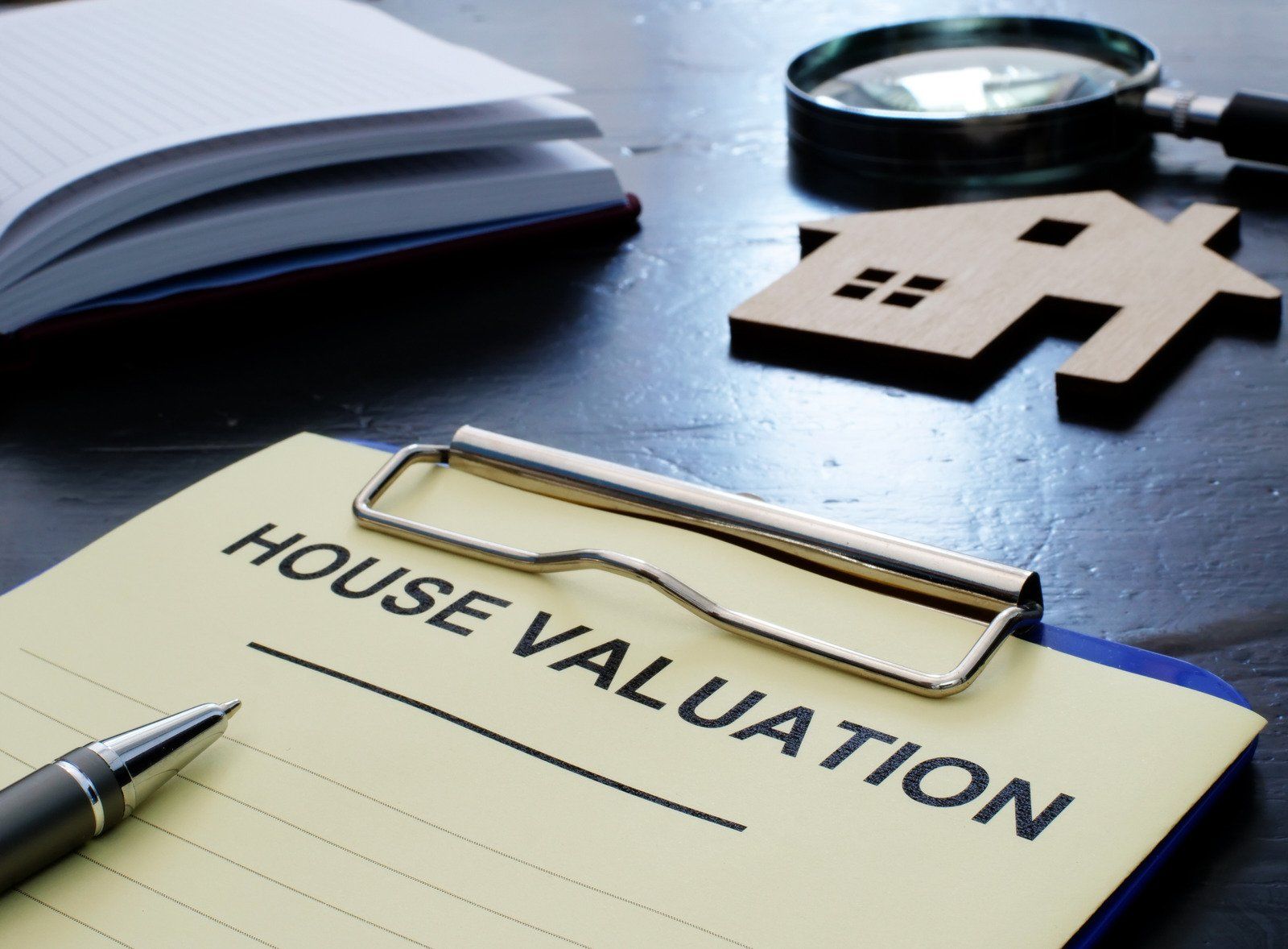 House valuation form with a model house, pen, notepad, and magnifying glass.