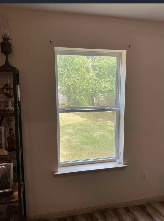 Interior room with a single white-framed window overlooking green trees and lawn.