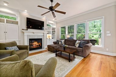 Bright living room with fireplace, sectional sofa, armchairs, large windows, and hardwood floors