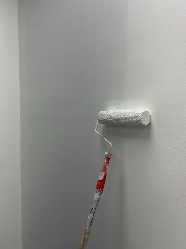 Paint roller applying white paint to a gray wall