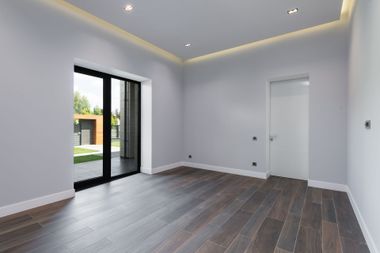 Empty modern room with gray walls, wood floor, recessed lights, and open glass doors to a patio