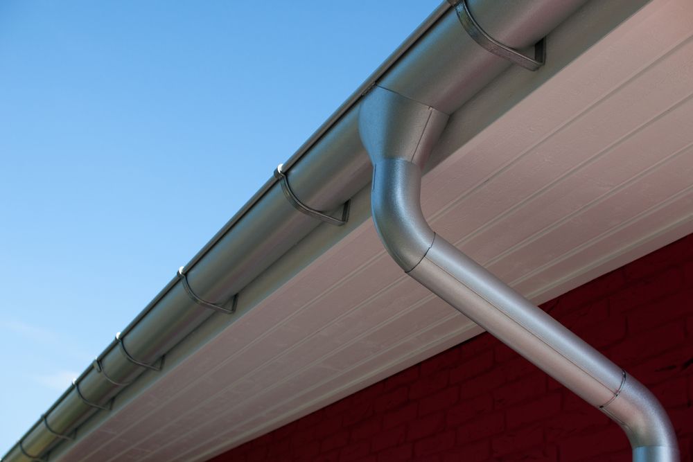 Silver Gutters on a Red Building With White Siding Against a Clear Blue Sky — Darren Smith Roofing In Glendale, NSW