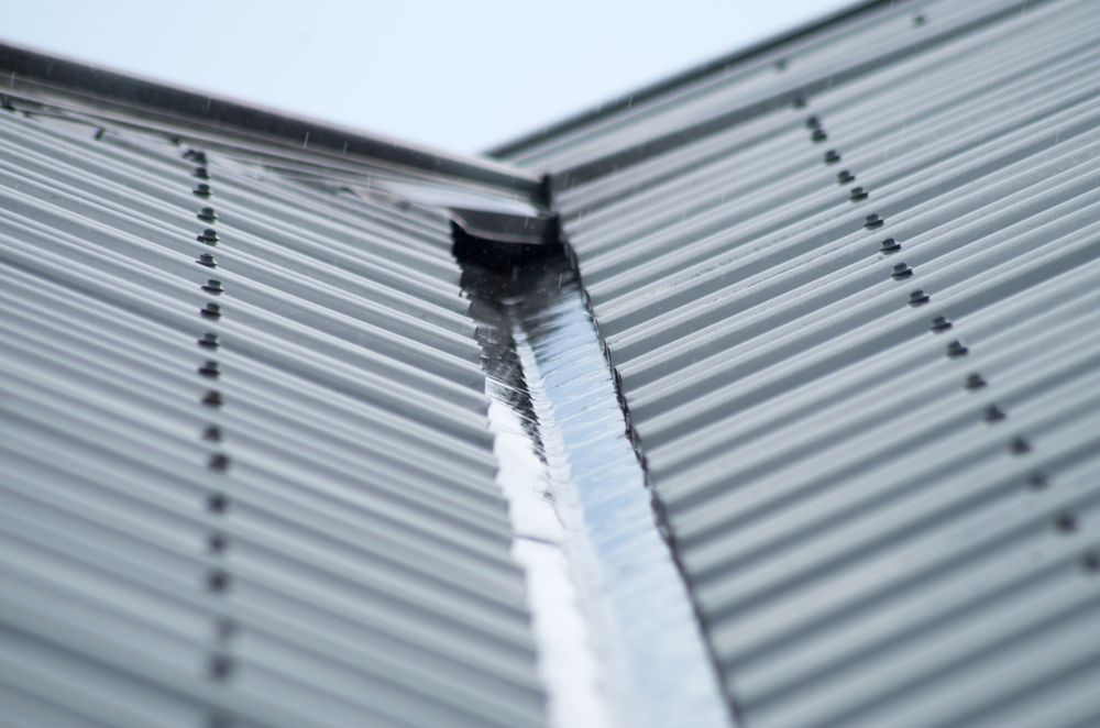 Metal roof with rainwater flowing into a gutter.