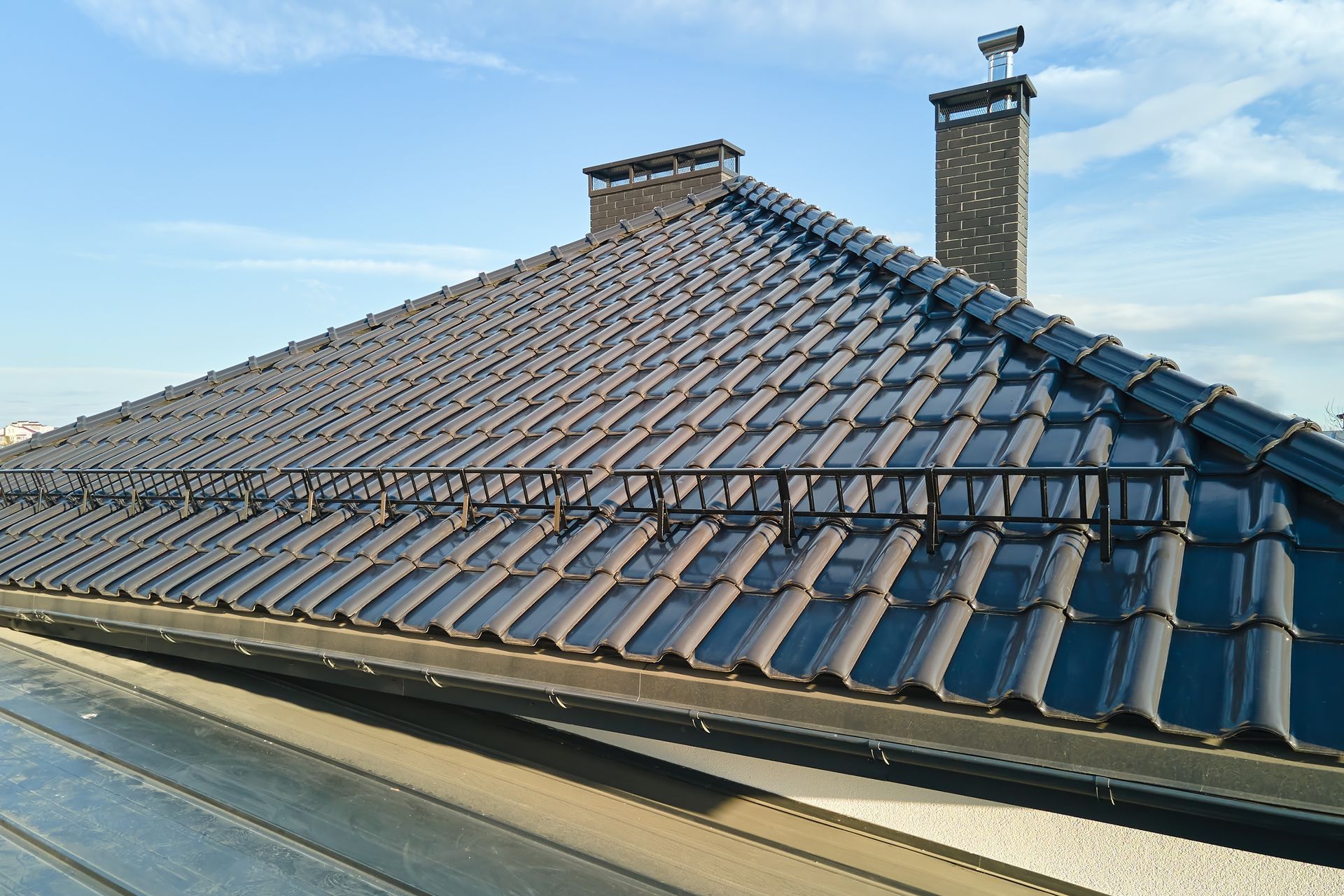 Dark Tiled Roof With Chimney Against a Blue Sky — Darren Smith Roofing In Kotara, NSW