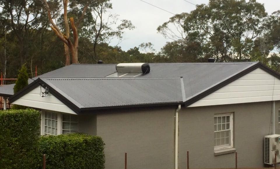 Grey House With Dark Corrugated Roof, Solar Water Heater, and White Trim — Darren Smith Roofing In Glendale, NSW